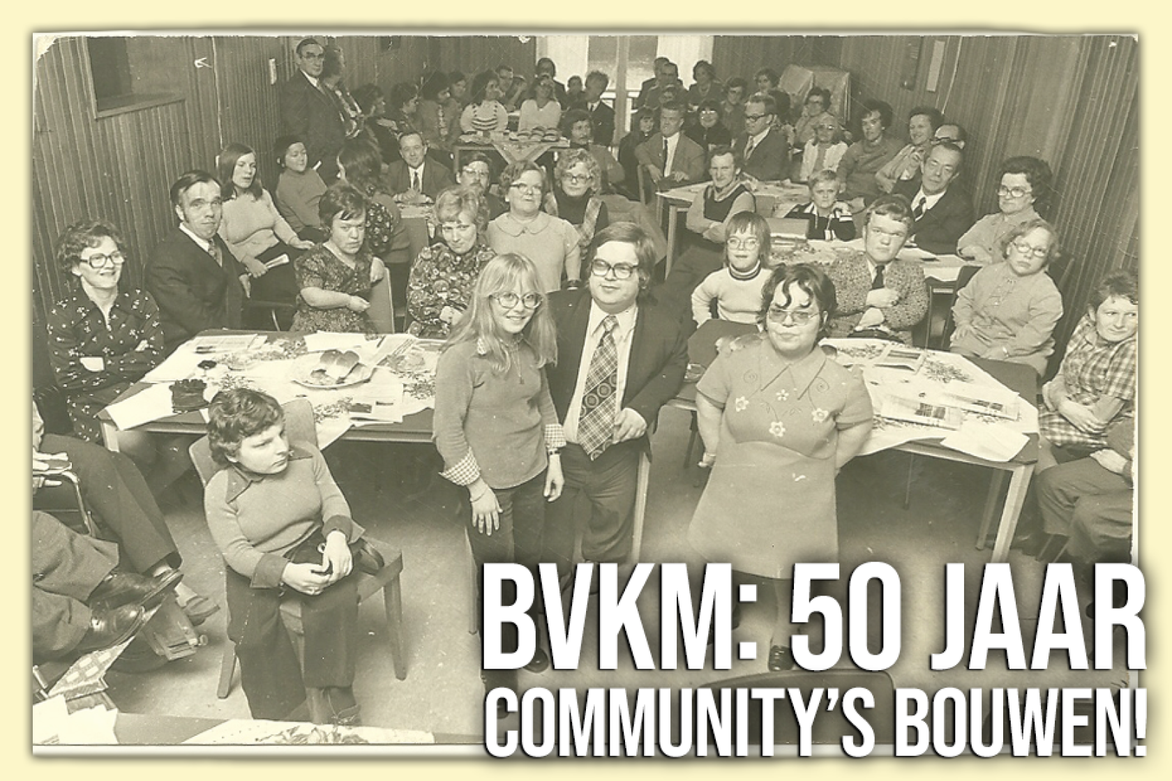 Historische zwart-witfoto van een bijeenkomst met volwassenen en kinderen aan tafels, ter gelegenheid van 50 jaar communityvorming bij BVKM.