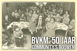 Historische zwart-witfoto van een bijeenkomst met volwassenen en kinderen aan tafels, ter gelegenheid van 50 jaar communityvorming bij BVKM.